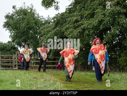 I partecipanti in abiti eleganti prendono parte alla Marathon Du Malton, a Malton, nel North Yorkshire. La corsa delle 10K è ispirata alla famosa Marathon Du Medoc nella regione vinicola francese. In linea con l'amore della città per i prodotti freschi, molti partecipanti si vestono come cibo. Data foto: Domenica 15 settembre 2024. Foto Stock