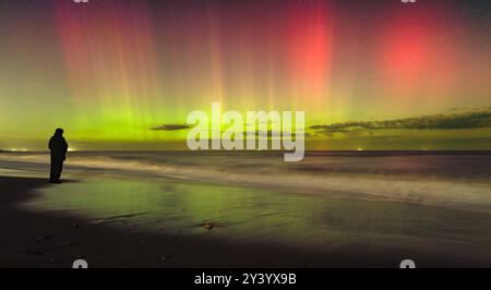 La spettacolare aurora boreale balla sulla spiaggia di Happisburgh nel Norfolk mentre una persona sola guarda con stupore Foto Stock