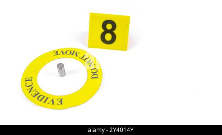 Un involucro di proiettile esaurito, posizionato all'interno di un cerchio giallo, etichettato con la prova del testo, non si muove, con un'etichetta con numero 8 sfocata, posta contro un bac bianco Foto Stock