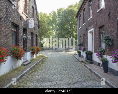 Pittoresca strada acciottolata con vecchie case e fiori, circondata da alberi, krudenburg, huenxe, basso reno, germania Foto Stock