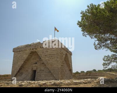 Edificio in pietra con una bandiera sul tetto, circondato dalla natura sotto un cielo blu brillante, sa coma, maiorca, spagna Foto Stock