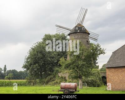 Vecchio mulino a vento in un villaggio con nuvole nel cielo e un trattore in primo piano, Huenxe, basso Reno, Germania, Europa Foto Stock