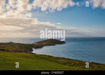 Una vista panoramica della costa caratterizzata da colline verdi che conducono giù verso l'oceano. Il cielo è parzialmente nuvoloso con macchie blu, e una piccola isola è visib Foto Stock