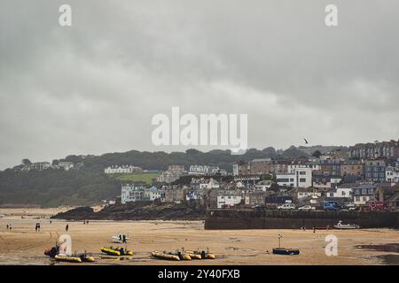 Una scena costiera caratterizzata da una spiaggia sabbiosa con diverse barche gialle ormeggiate in primo piano. Sullo sfondo, è ambientata una città con case ed edifici Foto Stock