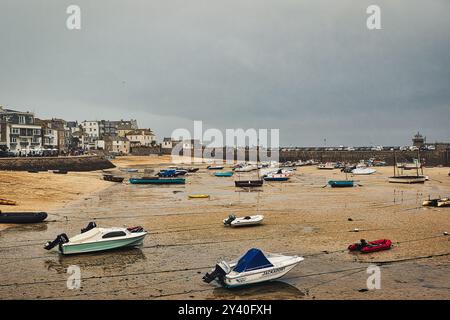 Una scena costiera con diverse barche ormeggiate in acque poco profonde con la bassa marea. Lo sfondo mostra una pittoresca cittadina di mare con edifici bianchi sotto un c Foto Stock
