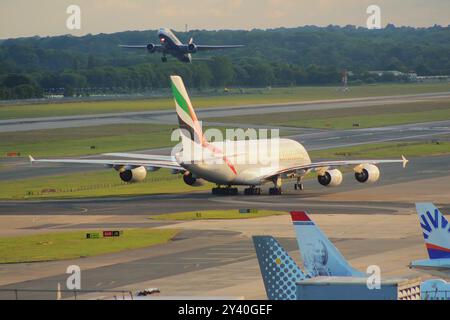Un taxi Emirates A380 sulla pista di rullaggio dopo l'atterraggio all'aeroporto di Gatwick, mentre un Boeing 777 della British Airways decolla dalla pista sullo sfondo. Foto Stock