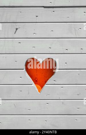 cuore rosso tagliato sul lato di una capanna in legno grigio chiaro Foto Stock