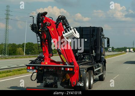 Gliwice, Polonia - 15 giugno 2023: Un camion robusto con una straordinaria gru idraulica rossa sta navigando lungo una trafficata autostrada, circondato da una vegetazione lussureggiante Foto Stock