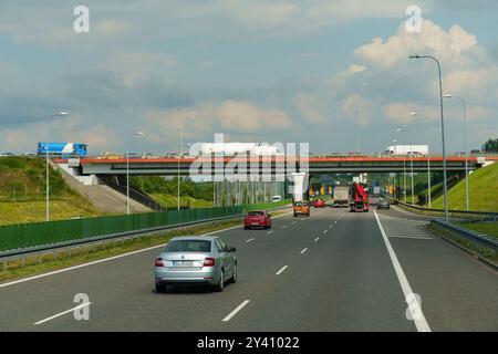 Gliwice, Polonia - 15 giugno 2023: Una vivace autostrada piena di veicoli viaggia sotto un cielo ampio, dove un cavalcavia incombe sopra, h Foto Stock