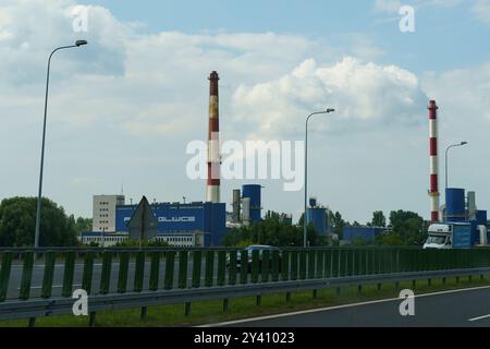 Gliwice, Polonia - 15 giugno 2023: L'animata area industriale di Gliwice presenta torreggianti ciminiere sullo sfondo di morbide nuvole, mentre il veicolo Foto Stock