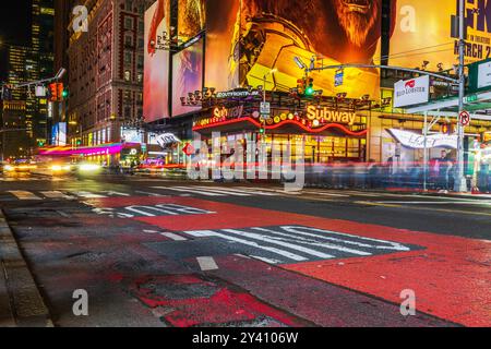 Vista notturna di Broadway di Manhattan sulla W42nd Street con grattacieli e la stazione della metropolitana 42nd Street, con sentieri leggeri da auto veloci. Nuovo Foto Stock