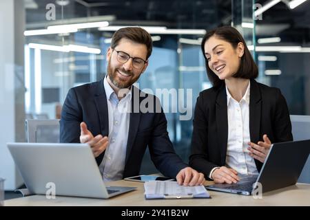 Professionisti aziendali impegnati in una discussione collaborativa utilizzando i laptop negli uffici moderni. Due colleghi condividono idee e lavorano al progetto. L'interazione sorridente mette in evidenza il lavoro di squadra Foto Stock