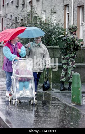 Una famiglia spinge una carrozza in un giorno di pioggia davanti a un soldato britannico che pattuglia l'area di Bogside, il 25 gennaio 1992 a Londonderry, Irlanda del Nord. Le forze di sicurezza hanno intensificato le pattuglie e le perquisizioni nella zona prima del ventesimo anniversario del massacro di Bloody Sunday. Foto Stock