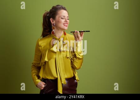 donna sorridente di 40 anni su sfondo verde con camicetta verde che utilizza lo smartphone. Foto Stock