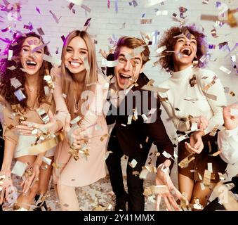 Amici multietnici che si divertono a vivere festeggiando con Falling Confetti Indoor Foto Stock