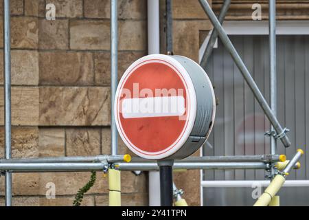 Un cartello rosso di divieto di ingresso montato su un palo, circondato da impalcature e un muro di pietra. Il segnale presenta una barra orizzontale bianca al centro, che indica Foto Stock