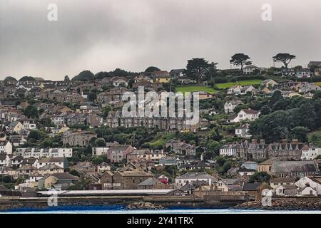 Una vista panoramica di una città collinare con case densamente affollate, che mostrano un mix di stili architettonici. Il paesaggio presenta colline verdi e nuvolose Foto Stock