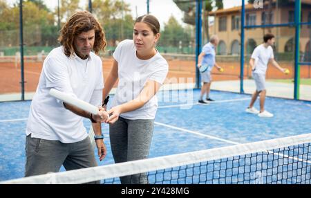Giovane coach che insegna a un uomo di mezza età a giocare a padel sul campo da tennis all'aperto Foto Stock