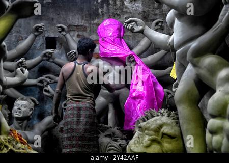 Kolkata, India. 14 settembre 2024. Un artista mette i tocchi di base a un idolo di Dea Durga, protetto da fogli di plastica per evitare il rischio di pioggia continua. Durga Puja, noto anche come Durgotsava o Sharodotsav, è un festival annuale che si svolge nel subcontinente indiano e che rende omaggio alla dea indù Durga, ed è anche celebrato a causa della vittoria di Durga su Mahishasura. (Foto di Avishek Das/SOPA Images/Sipa USA) credito: SIPA USA/Alamy Live News Foto Stock