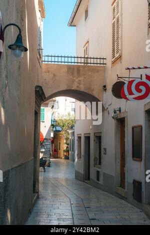 Strada stretta con un arco e cartelli per negozi nella città vecchia di Krk, Croazia. Foto Stock