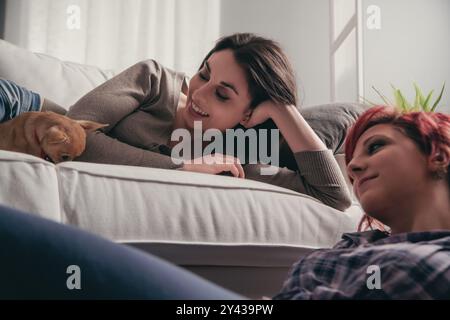 Amici intimi che ridono e si rilassano su un divano con il loro cane da compagnia, creando un'atmosfera calda nel loro soggiorno. I sorrisi genuini mostrano il loro profondo bon Foto Stock