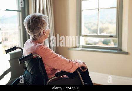 Pensare, casa e donna in sedia a rotelle per finestra con nostalgia, riflesso o memoria del passato. Demenza, pensionamento e anziana donna con Foto Stock