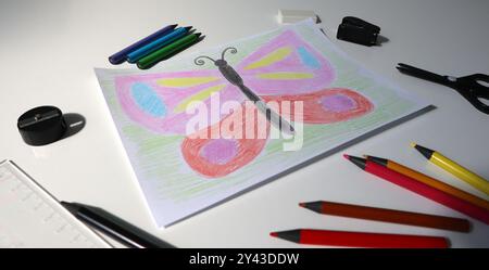 Foto del disegno del bambino con matite colorate in un angolo. Nell'immagine c'è la farfalla. Colori rosa, rosso, blu, verde. Apparecchiature per ufficio disponibili. Matite colorate, forbici, affilatrice, righello, ecc. Foto Stock