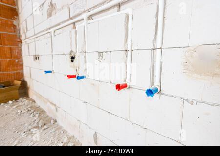 Nuovi tubi in PVC bianco esposti non finiti montati a parete. Le provette rosse e blu sono per l'acqua calda e fredda. Foto Stock