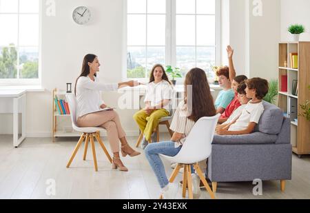 Gruppo di bambini seduti sul divano contro l'insegnante o lo psicologo, rispondendo o ponendo domande. Foto Stock