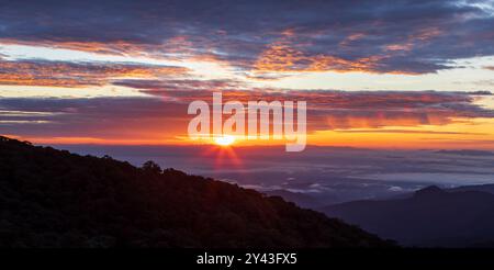 Vista panoramica delle montagne durante l'alba, il sole che sorge attraverso le spettacolari nuvole, la nebbia mattutina che scivola su una valle. Chiang mai, Thailandia. Foto Stock