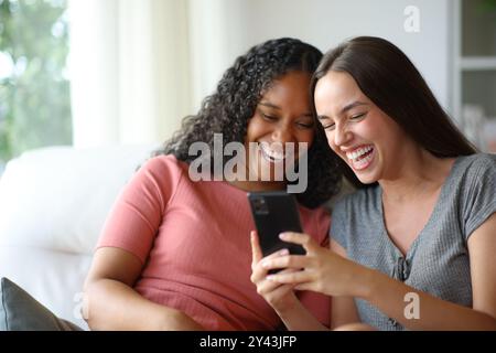 Le camere interrazziali felici ridono guardando i contenuti del telefono a casa Foto Stock