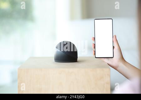 Primo piano di una donna che tiene in mano il modello dello schermo del telefono cellulare accanto all'altoparlante intelligente di casa Foto Stock