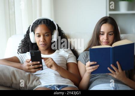 Il ritratto in prima visione di due coinquilini interrazziali, uno sta ascoltando musica e l'altro legge un libro di carta Foto Stock