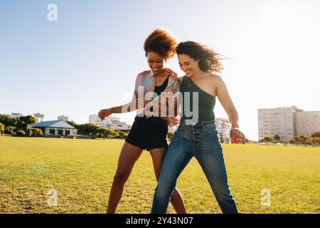Due giovani donne camminano gioiosamente attraverso un parco soleggiato, catturando un momento di amicizia e felicità in una splendida giornata estiva. Foto Stock