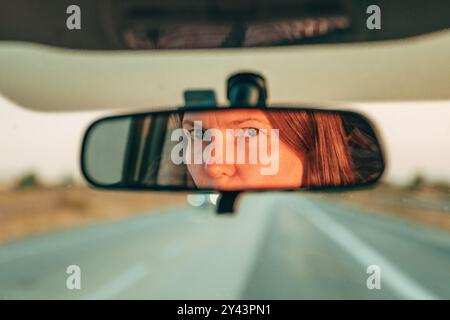 Siamo tornati da una vacanza di fine settimana. Gli occhi e il volto femminile del conducente si riflettono nello specchietto retrovisore dell'auto. Messa a fuoco selettiva. Foto Stock