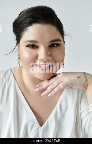 Una splendida sposa di grandi dimensioni mette in mostra la sua eleganza in un abito bianco che scorre, adornato da orecchini scintillanti. Foto Stock