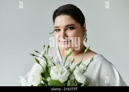 Una splendida sposa di grandi dimensioni sfoggia eleganza in un abito da sposa bianco e splendidi orecchini tenendo fiori freschi. Foto Stock