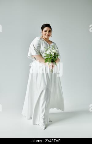 Una splendida sposa irradia fiducia in un abito bianco che scorre tenendo in mano un bellissimo bouquet. Foto Stock