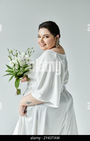 Una splendida sposa irradia gioia mentre tiene in mano un bouquet, mostrando il suo grazioso abbigliamento da sposa. Foto Stock