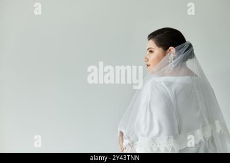 Una splendida sposa con un abito bianco e eleganti orecchini irradia bellezza su un morbido sfondo grigio. Foto Stock