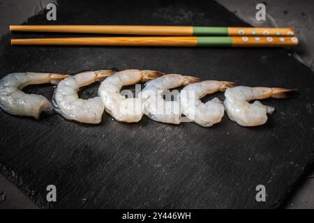 Gamberi crudi di re o tigre disposti in fila con bacchette su una tavola di mica nera, spazio Copia. Foto di alta qualità Foto Stock