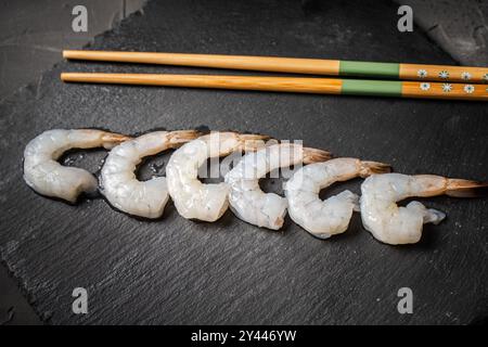 Gamberi crudi di re o tigre disposti in fila con bacchette su una tavola di mica nera, spazio Copia. Foto di alta qualità Foto Stock