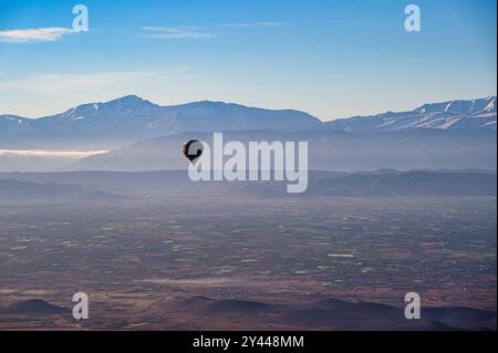 Una mongolfiera rossa, che galleggia sul deserto vicino a Marrakech, in Marocco, in una limpida giornata primaverile, con le montagne innevate dell'Atlante sullo sfondo Foto Stock