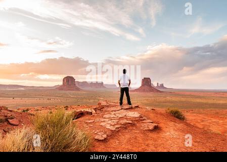 Uomo in piedi su una sporgenza che si affaccia sulla Monument Valley al tramonto. Foto Stock