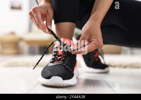 Donna con lacci di scarpe da ginnastica in interni, primo piano Foto Stock