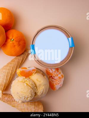 Una tazza di gelato accanto a un cono di gelato e alle arance su una superficie beige Foto Stock