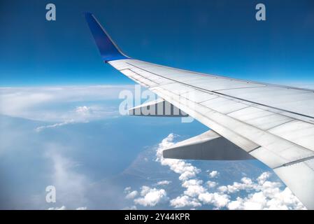 Ala di un aereo che si innalza sopra soffici nuvole contro un cielo blu in una giornata di sole, evocando pensieri di viaggio, libertà e vacanze estive Foto Stock