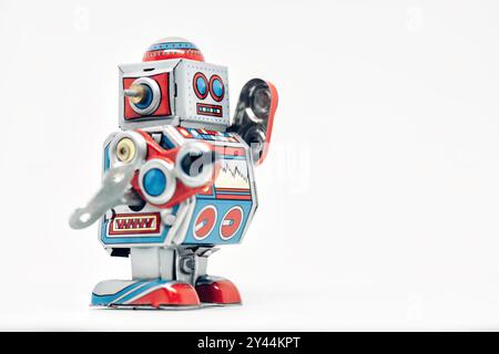 Il robot giocattolo classico si stende su uno sfondo bianco e ondeggia con il braccio rosso sollevato Foto Stock