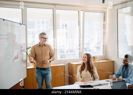Una vivace discussione si svolge in un ufficio contemporaneo, mentre un leader maturo e gioviale condivide un momento di spensieratezza con un team diversificato, favorendo un'atmosfera di brainstorming rilassata ma produttiva Foto Stock