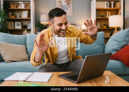 Uomo che sta ricevendo una videochiamata da casa, sorridente e saluta Foto Stock